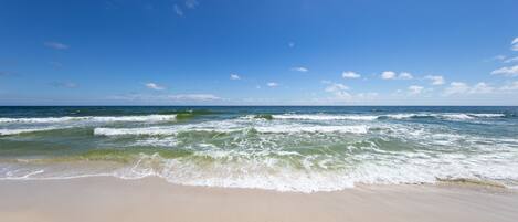Ein Strand mit Wellen, blauem Himmel und weiter Ferne.