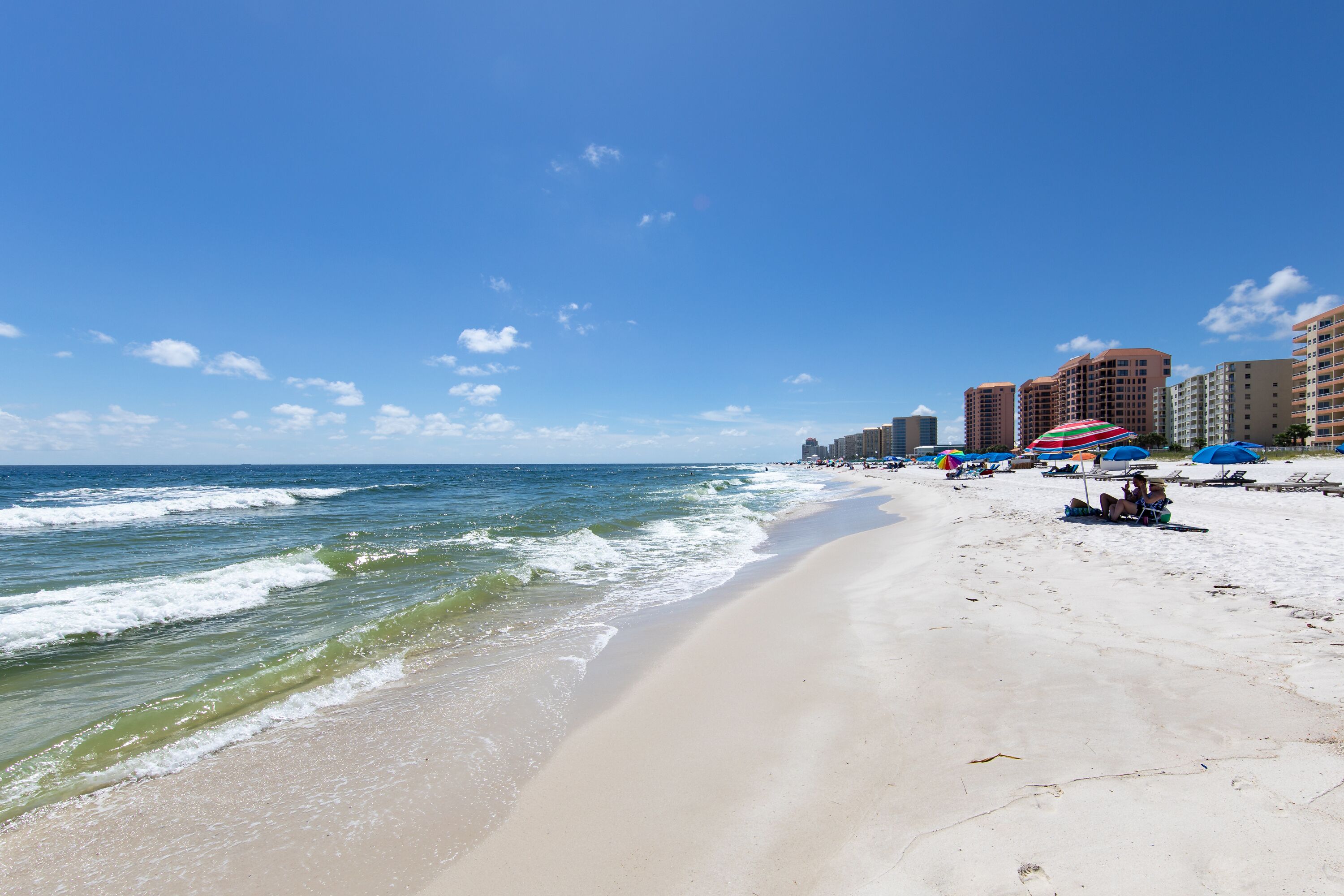 A beach with a sandy shore, ocean waves, and buildings in the background.