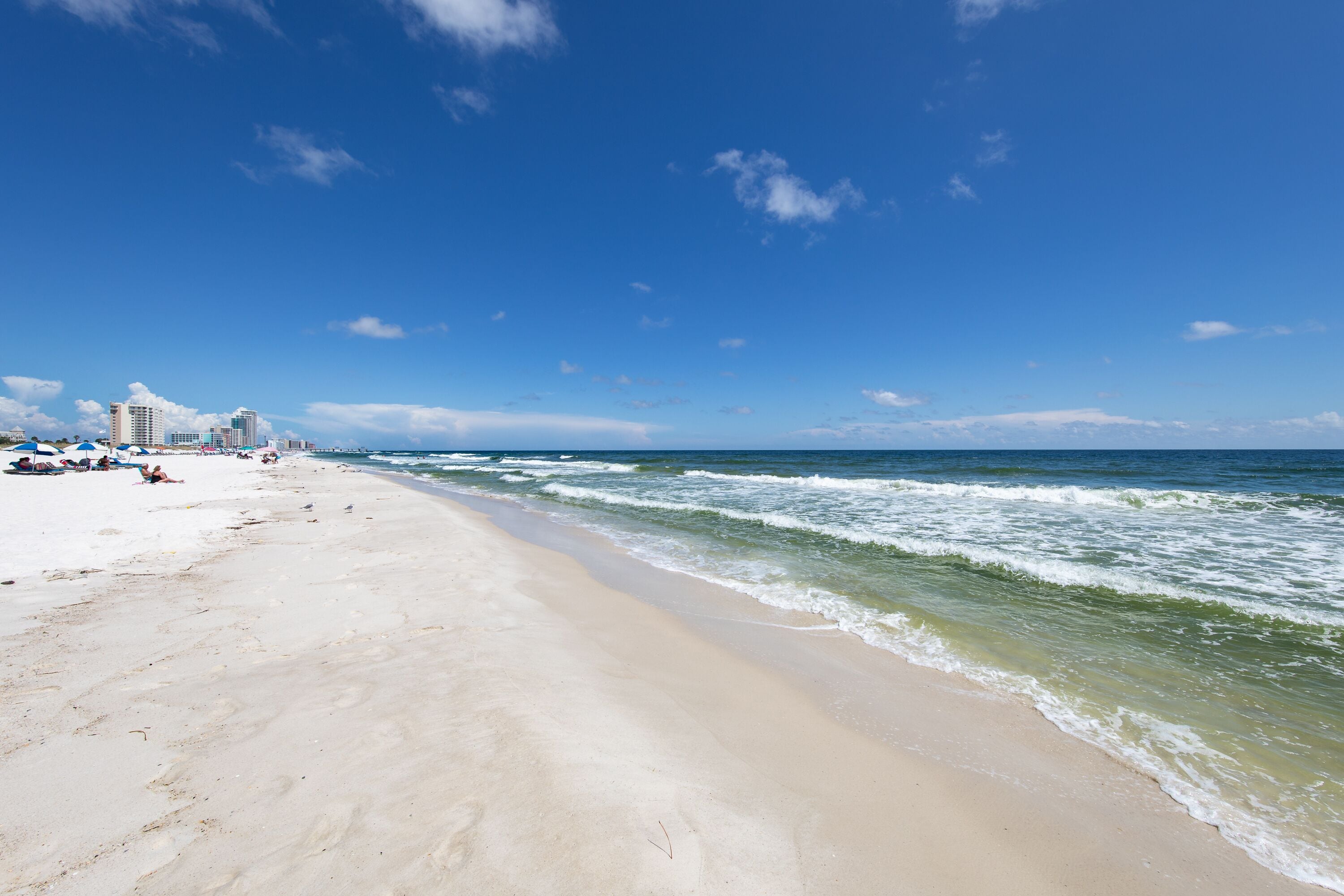 A beach with a sandy shore, ocean waves, and a clear blue sky.