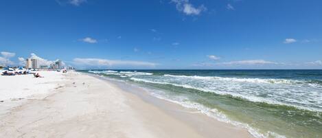 A beach with a sandy shore, ocean waves, and a clear blue sky.