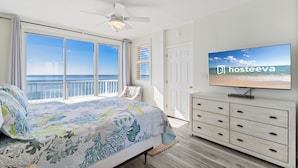 Un dormitorio con una ventana grande, una cama, un televisor y un aparador de madera.