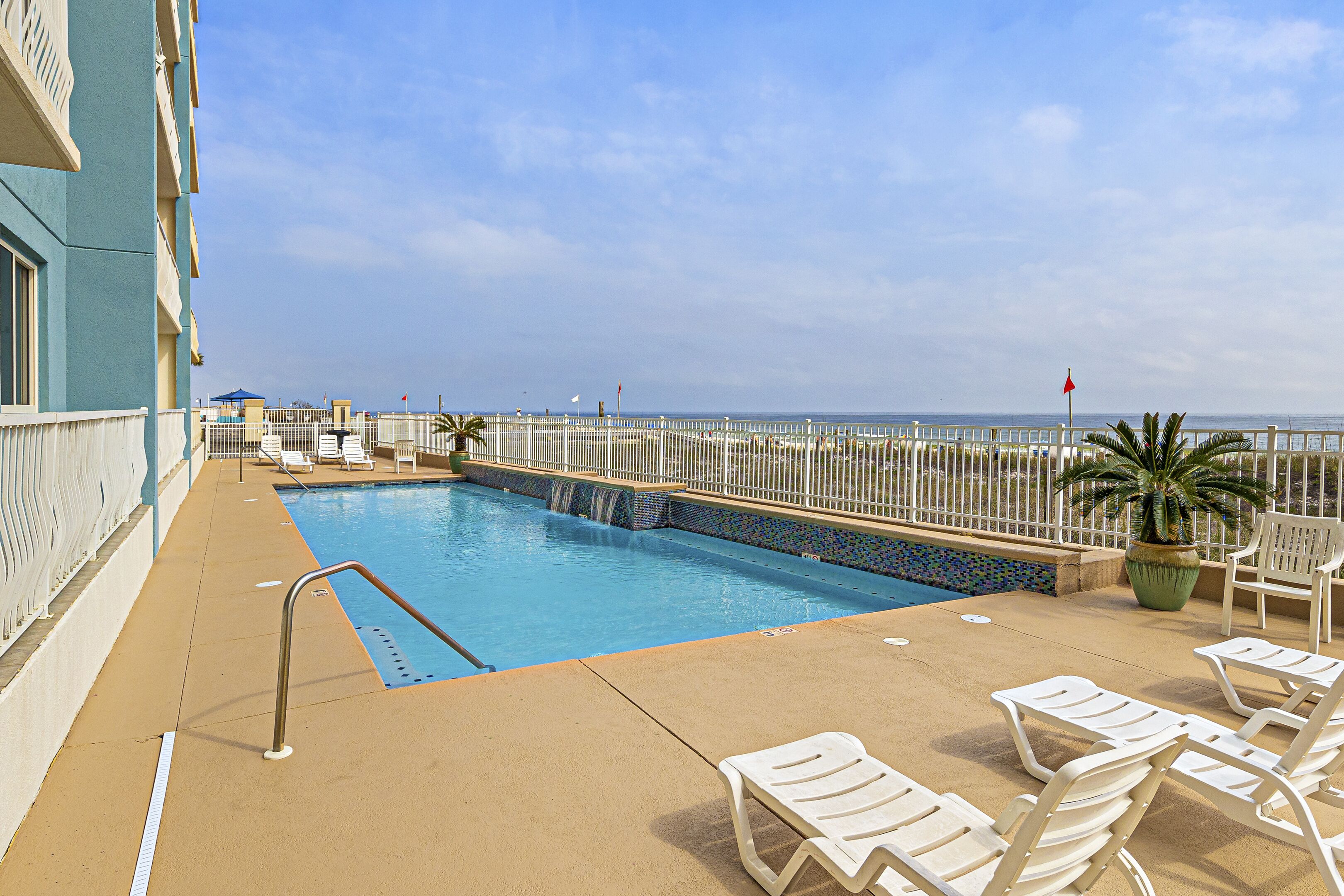 A pool area with lounge chairs and a view of the ocean.