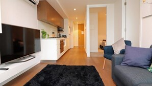 Ein modernes Wohnzimmer mit Flachbildfernseher, schwarzem Teppich, grauem Sofa und einer Küchenzeile mit weißen Schränken und Herd.