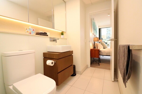 Ein modernes Badezimmer mit Toilette, Waschbecken und Spiegel. Ein Handtuchhalter und eine kleine Pflanze stehen auf der Ablagefläche.