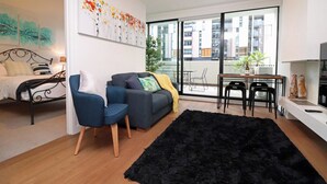Ein modernes Wohnzimmer mit einer Couch, Sesseln, einem schwarzen Teppich, einem Esstisch und einem Fernseher.