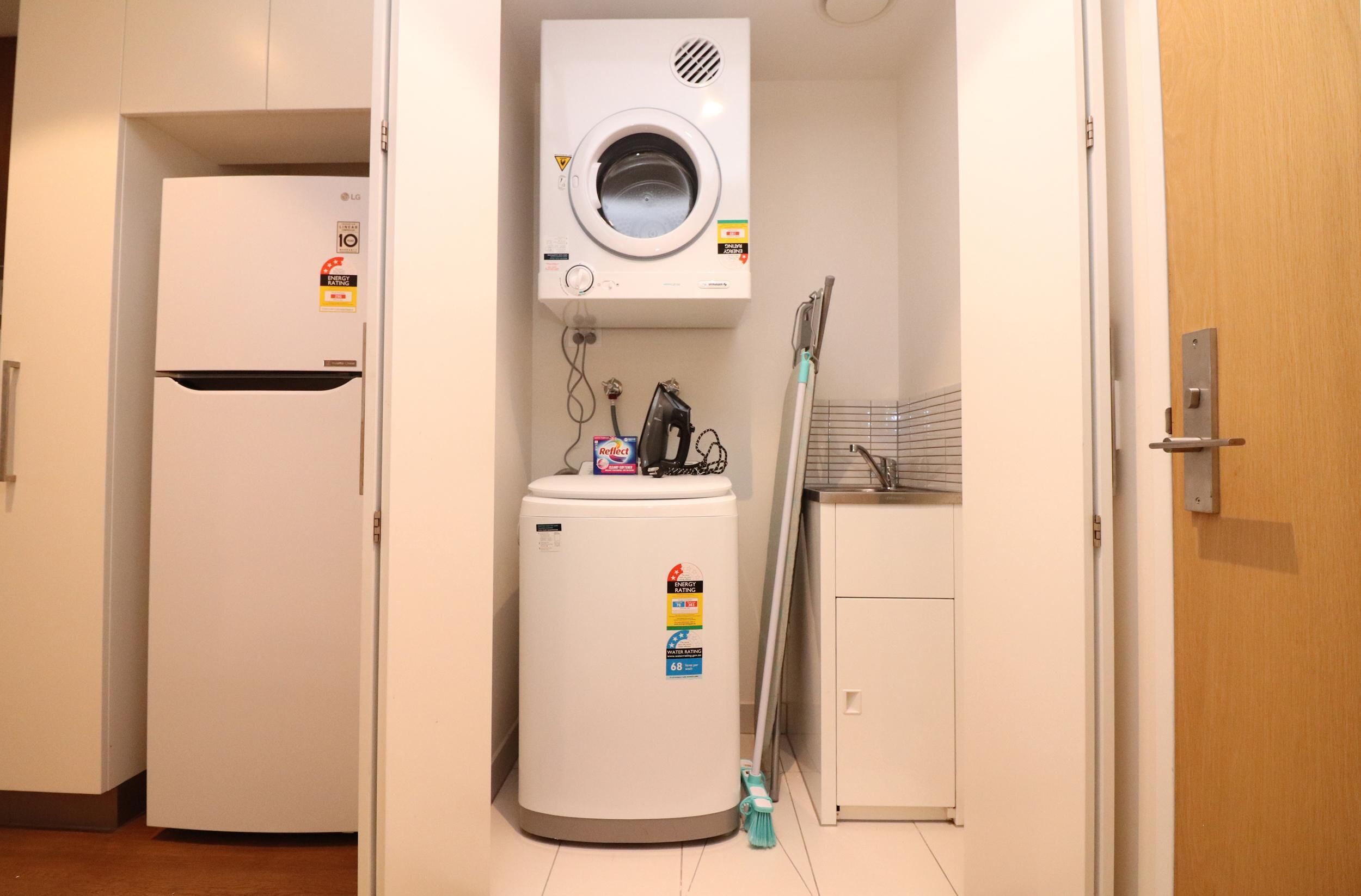 Cocina compacta con lavadora integrada, refrigerador y un lavamanos pequeño.
