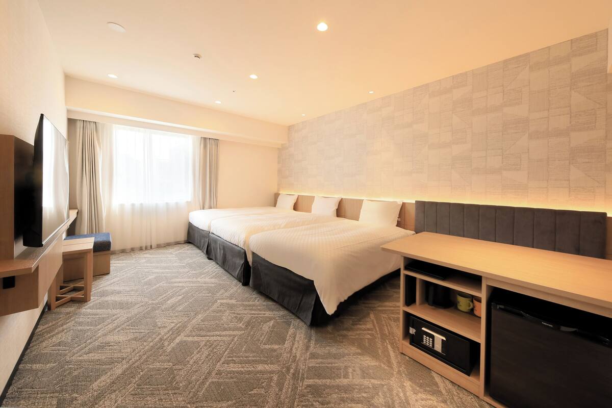 A hotel room with two beds, a TV, a desk, and a refrigerator.