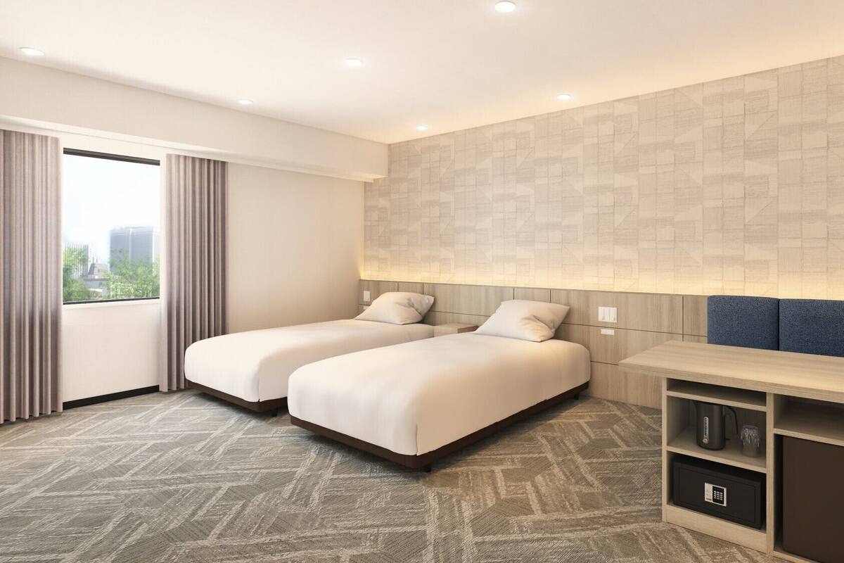 A hotel room with two beds, a large window with curtains, a wall-mounted TV, a minibar, and a patterned carpet.