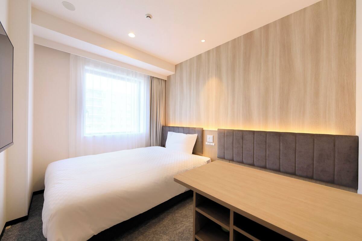 A hotel room with a large bed, a desk, and a wall-mounted TV.