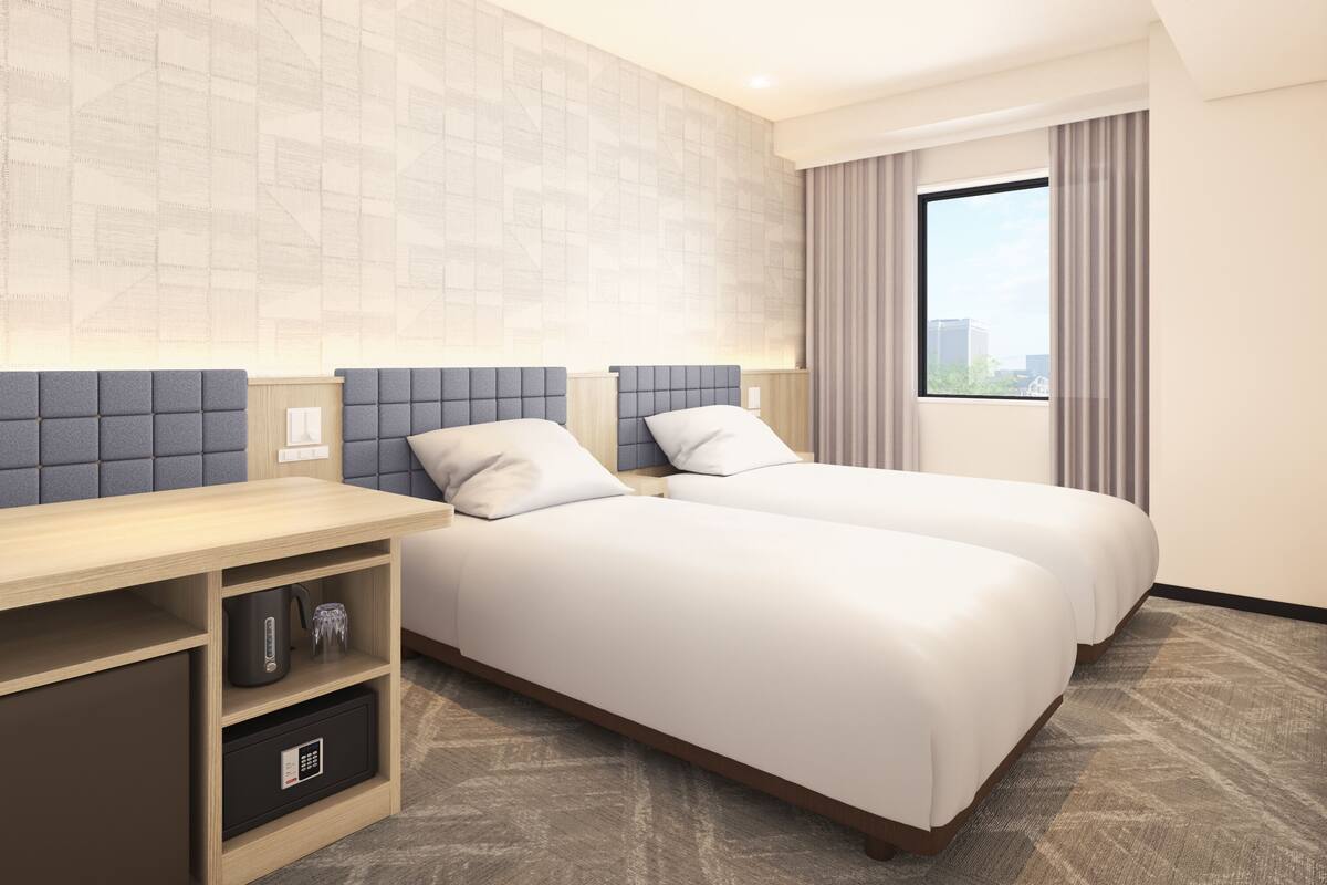 A hotel room with two beds, a desk, a safe, and a window with curtains.