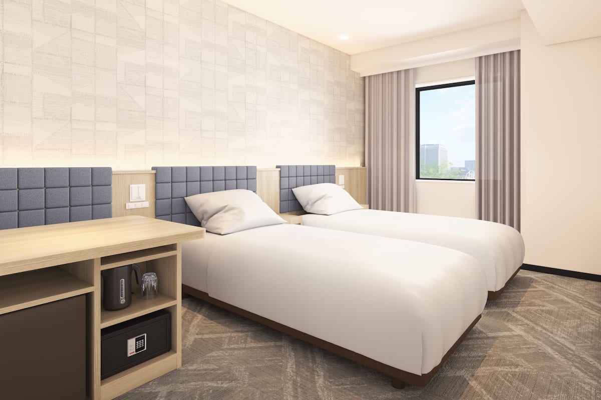 Habitación de hotel con dos camas, un escritorio, una caja fuerte y una ventana con cortinas.