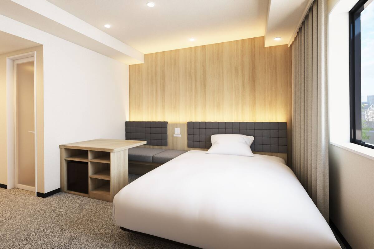 A hotel room with a bed, a small desk, a wardrobe, and a window with a view.
