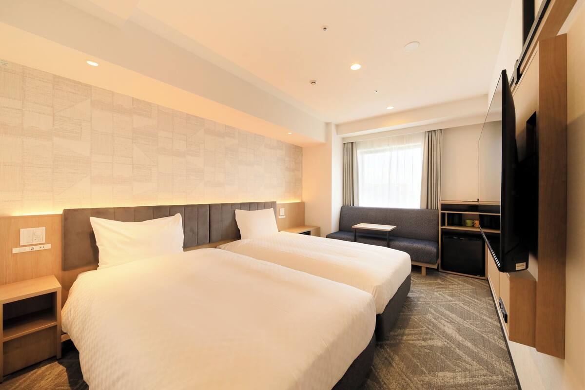 A hotel room with two beds, a television, a desk, and a window with curtains.