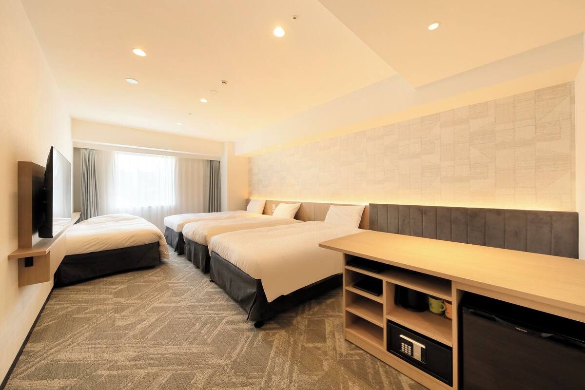 A hotel room with two beds, a TV, a desk, and a refrigerator.