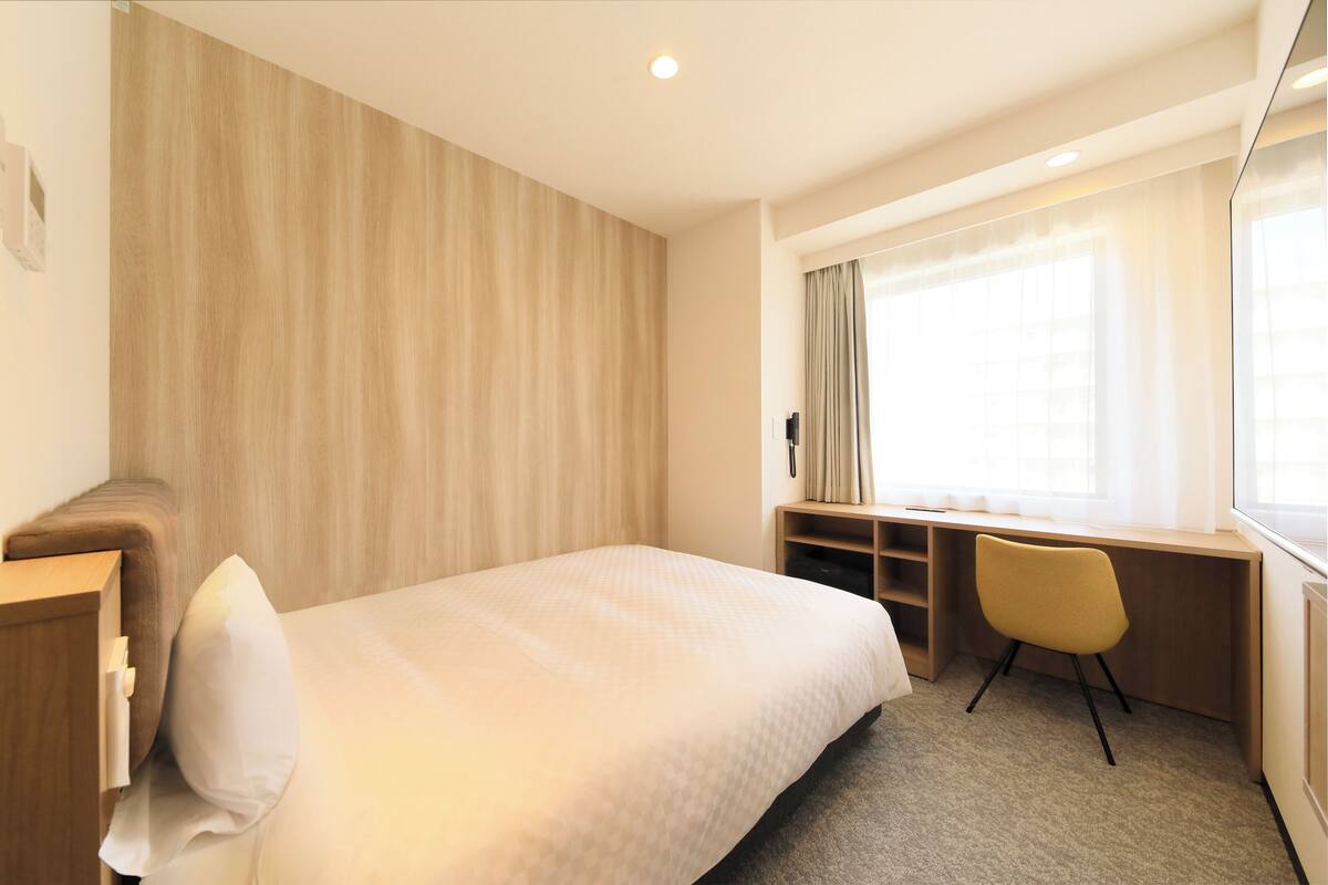 A hotel room with a bed, a desk, a chair, and a large window with curtains.