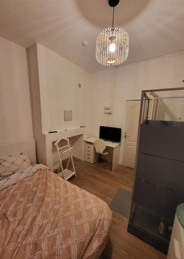 A bedroom with a bed, a desk, a chair, a TV, and a wardrobe.