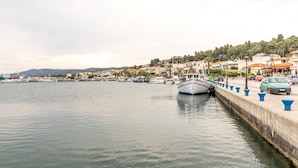 A waterfront marina with boats docked, a concrete quay with blue bollards, and buildings in the background. - Mina-Maria Apartments (Kassandra)