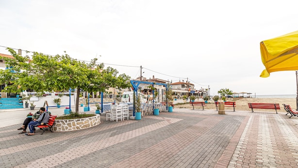 A paved promenade with benches, potted plants, and a blue structure. - Mina-Maria Apartments (Kassandra)