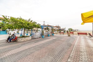 A paved promenade with benches, potted plants, and a blue structure. - Mina-Maria Apartments (Kassandra)