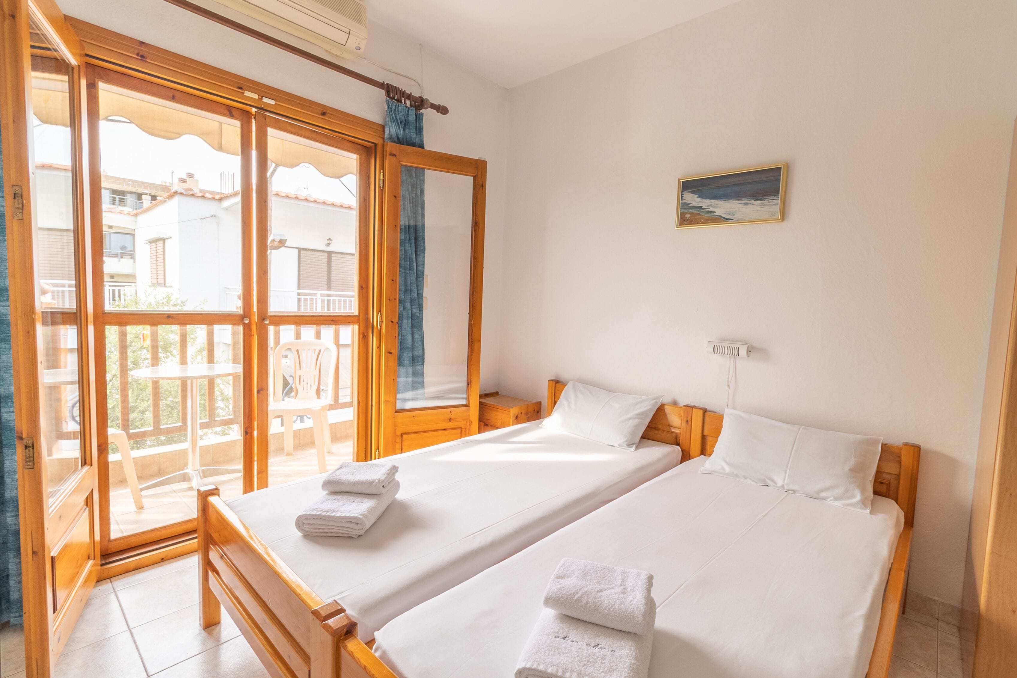 A room with two beds, a balcony, and a painting on the wall.