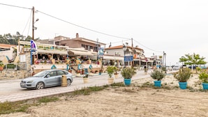 A street with a car parked on the side, buildings with shops, and potted plants. - Mina-Maria Apartments (Kassandra)