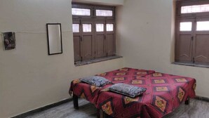 A small, simple room with a single bed, two windows, and a wall-mounted light fixture. - A perfect stay for family & friends. (VARANASI)