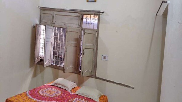 A bedroom with a bed, a wardrobe, and a window with a metal grill. - A perfect stay for family & friends. (VARANASI)