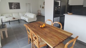 En moderne stue med en hvid sofa, et træspisebord med stole, og et køkkenområde med mikroovn og ovn.