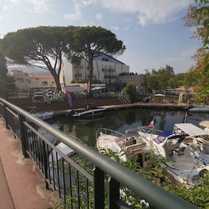 A marina with boats docked, a building with balconies, and a tree in the foreground.