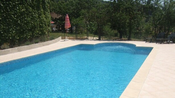 A rectangular swimming pool with clear blue water, surrounded by a tiled deck and shaded by trees. - Beautiful independent cottage with garden (Contes)