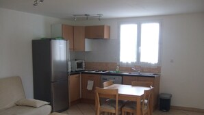 A compact kitchen with a refrigerator, microwave, and sink. There is a dining table with chairs and a sofa in the living area. - Beautiful independent cottage with garden (Contes)