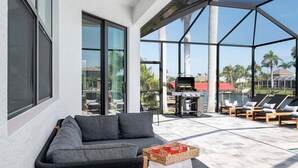 Ein moderner Außenbereich zum Verweilen mit einer Couch, Lounge-Stühlen, einem Grill und Blick auf Palmen.