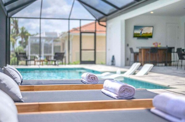 Zona junto a la piscina con sillones de descanso y toallas, una piscina y un área de comedor con sillas y una mesa.