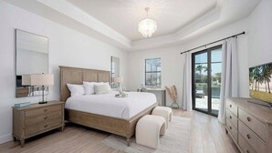 Ein Schlafzimmer mit einem großen Bett, Nachttischen, einer Chandelier und Blick ins Freie.
