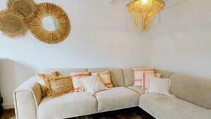 Una sala de estar moderna con un sofá seccional color beige, detalles decorativos de tejido en la pared y una lámpara colgante.