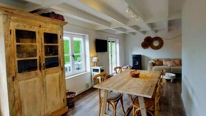 Un comedor con mesa y sillas de madera, un armario de madera con puertas de cristal, un televisor montado en la pared y un sofá al fondo.