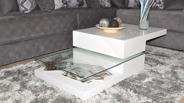Ein stilvolles Wohnzimmer mit einem grauen Sofa, einem weißen Couchtisch mit Glasplatte und Dekorationselementen.