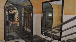 Eine Lobby mit Glastür und Metallgeländern, eine Treppe mit Handlauf sowie ein gefliester Boden.
