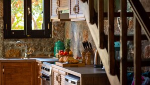 A kitchen with wooden cabinets, a stone wall, and a window with blinds. - Carob Cottage (Plaka Elounda)