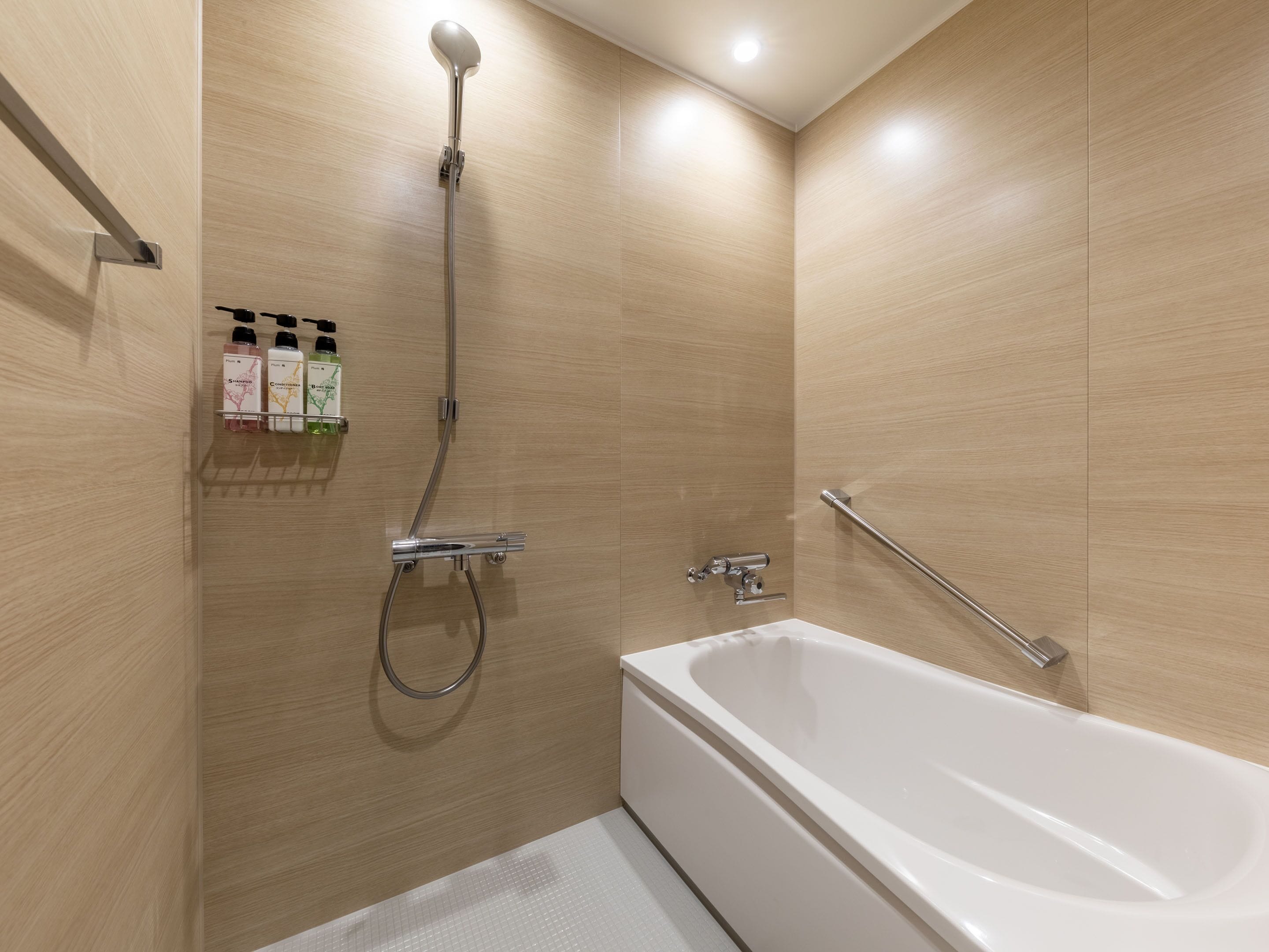 A modern bathroom with a white bathtub, a showerhead, and a handrail.
