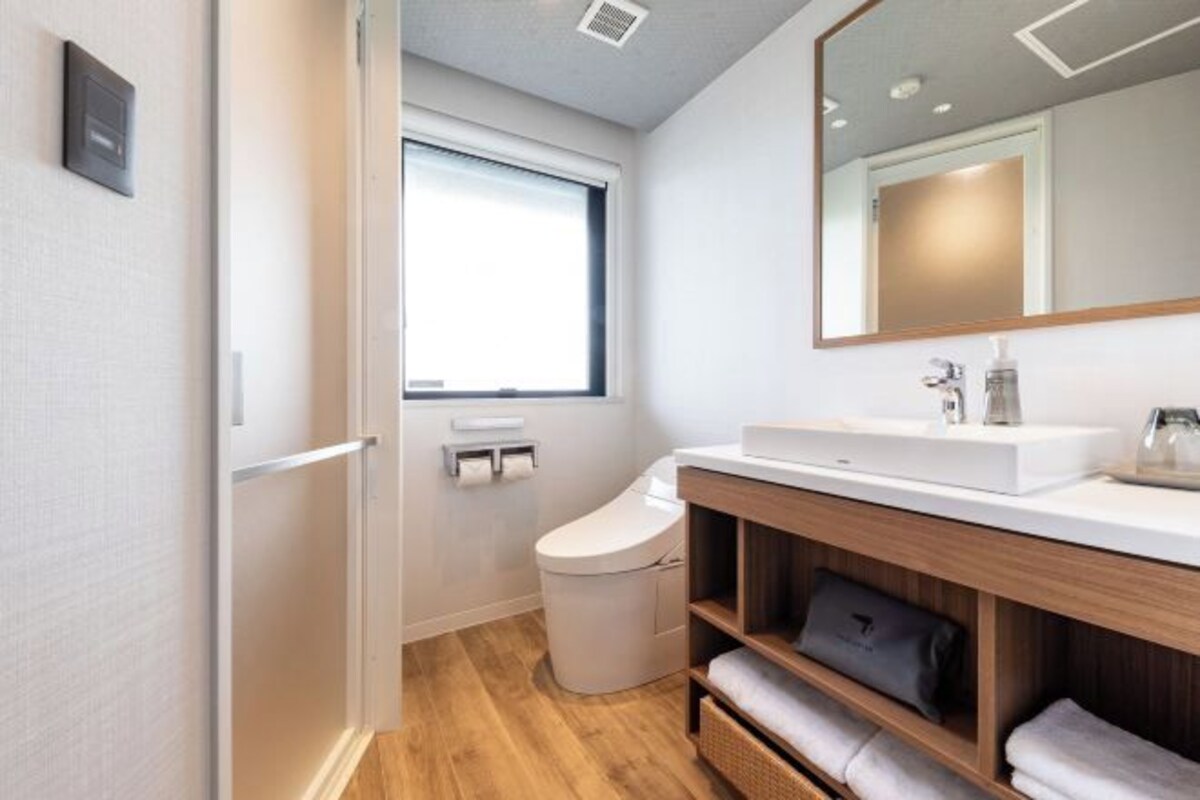 Un baño moderno con un lavamanos blanco, tocador de madera y un espejo grande.
