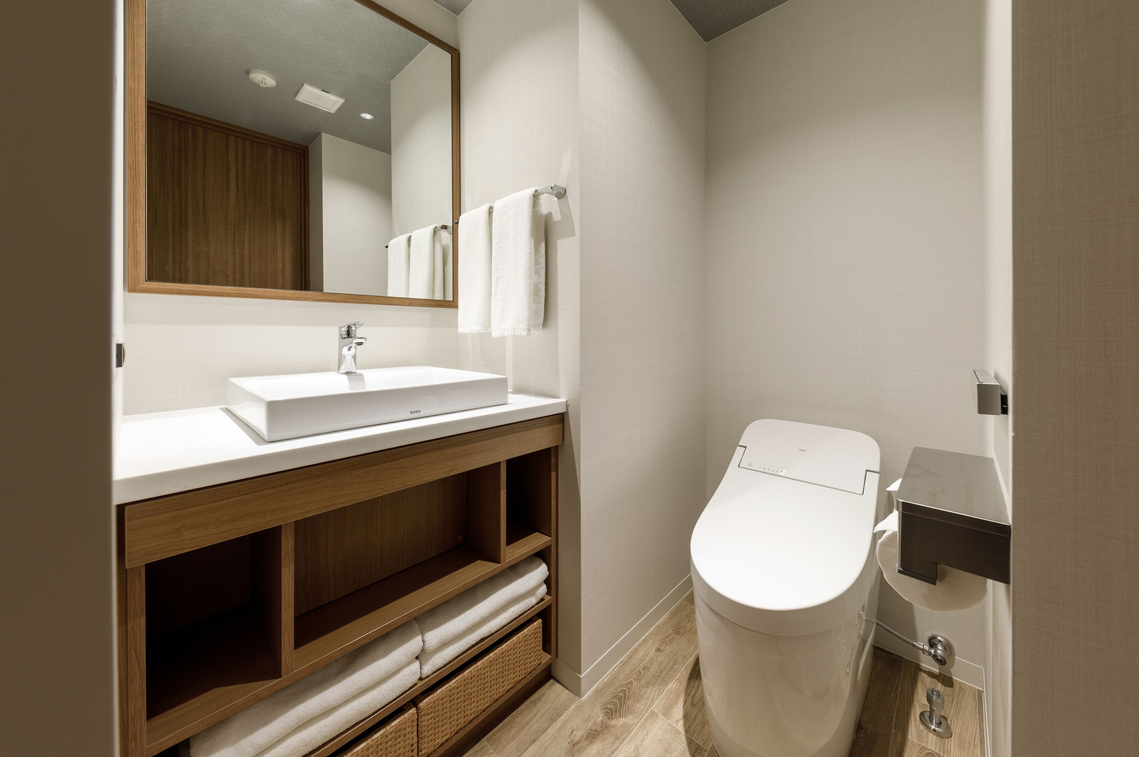 Un baño moderno con lavamanos blanco, tocador de madera y retrete.