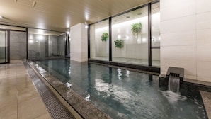 A modern indoor swimming pool with clear glass walls, a tiled floor, and a water feature.