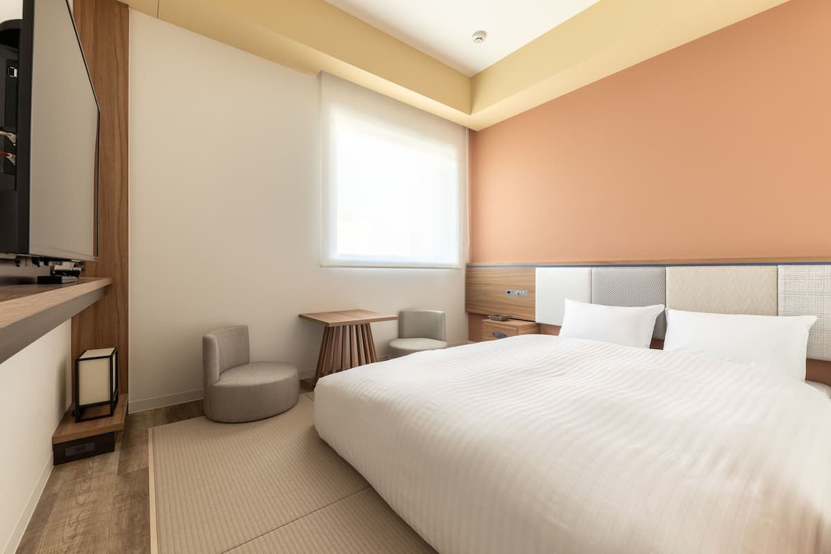 Ein modernes Hotelzimmer mit einem großen Bett, einem kleinen runden Tisch, einem Fernseher und einem Fenster.