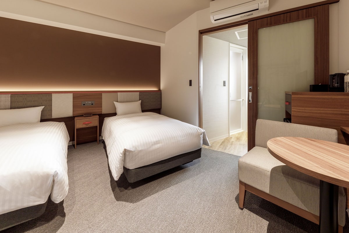Ein Hotelzimmer mit zwei Betten, einem Schreibtisch, einem Stuhl und einer Klimaanlage.