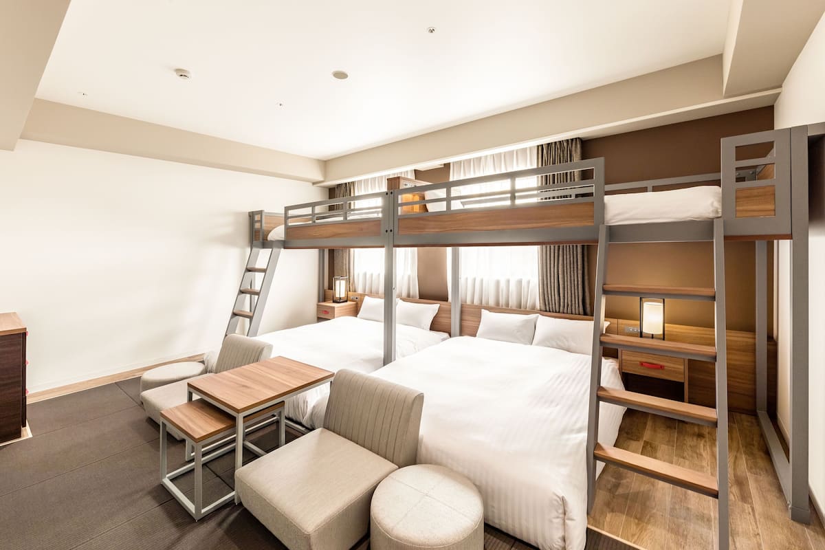 Ein modernes Hotelzimmer mit Stockbetten, einem Schreibtisch, einem Stuhl und einem kleinen Tisch.