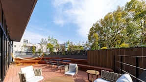An outdoor patio with a hammock, seating area, and a view of trees and buildings.