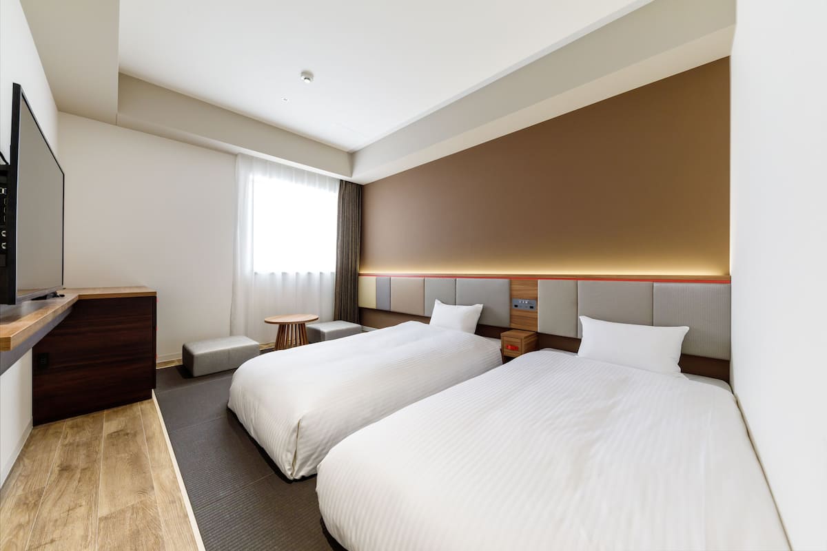 Ein Hotelzimmer mit zwei Betten, einem Schreibtisch, einem Fernseher und einem Fenster mit Vorhängen.