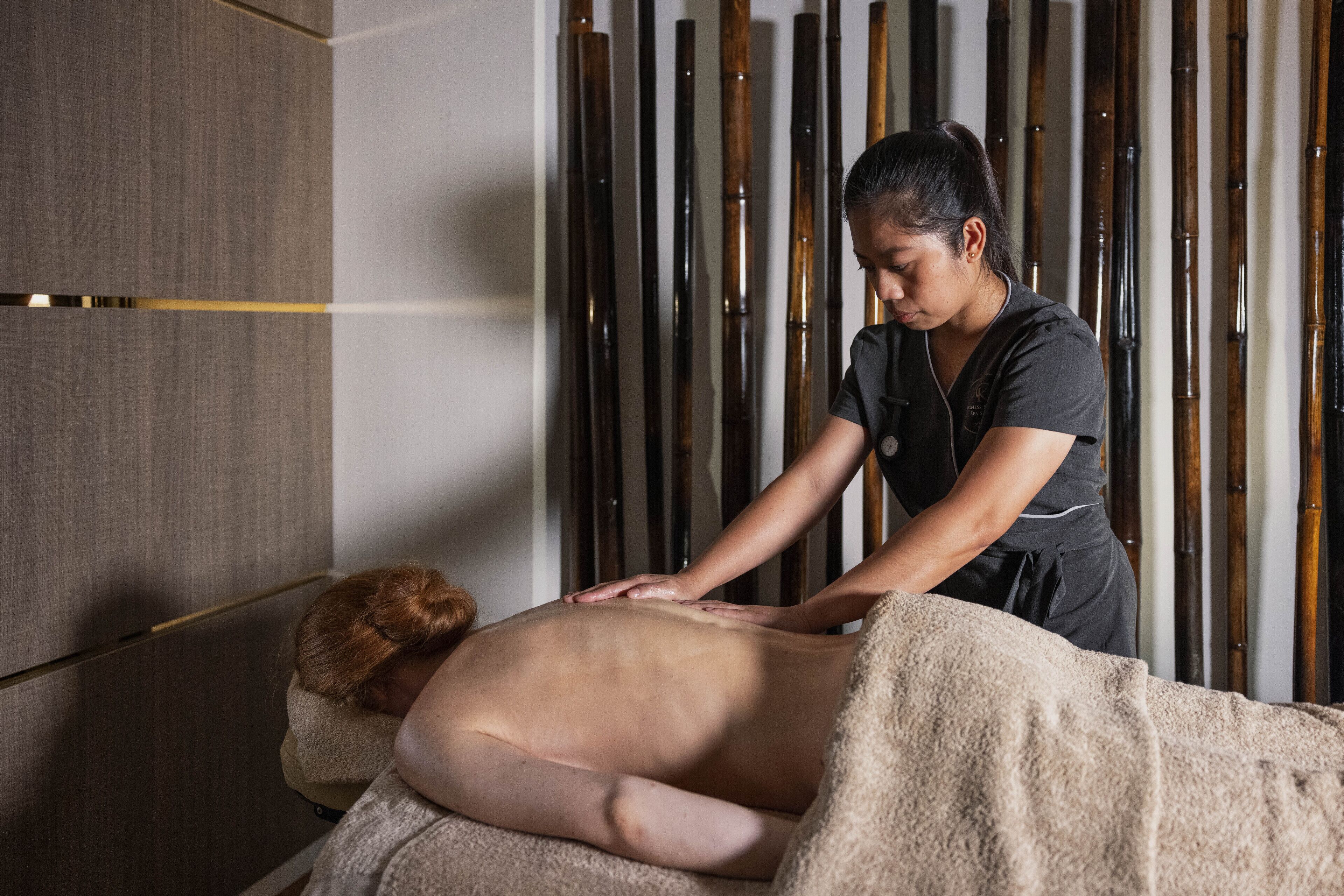 Une séance de massage dans un espace au design moderne, avec un mur revêtu de panneaux en bois et une table de massage.