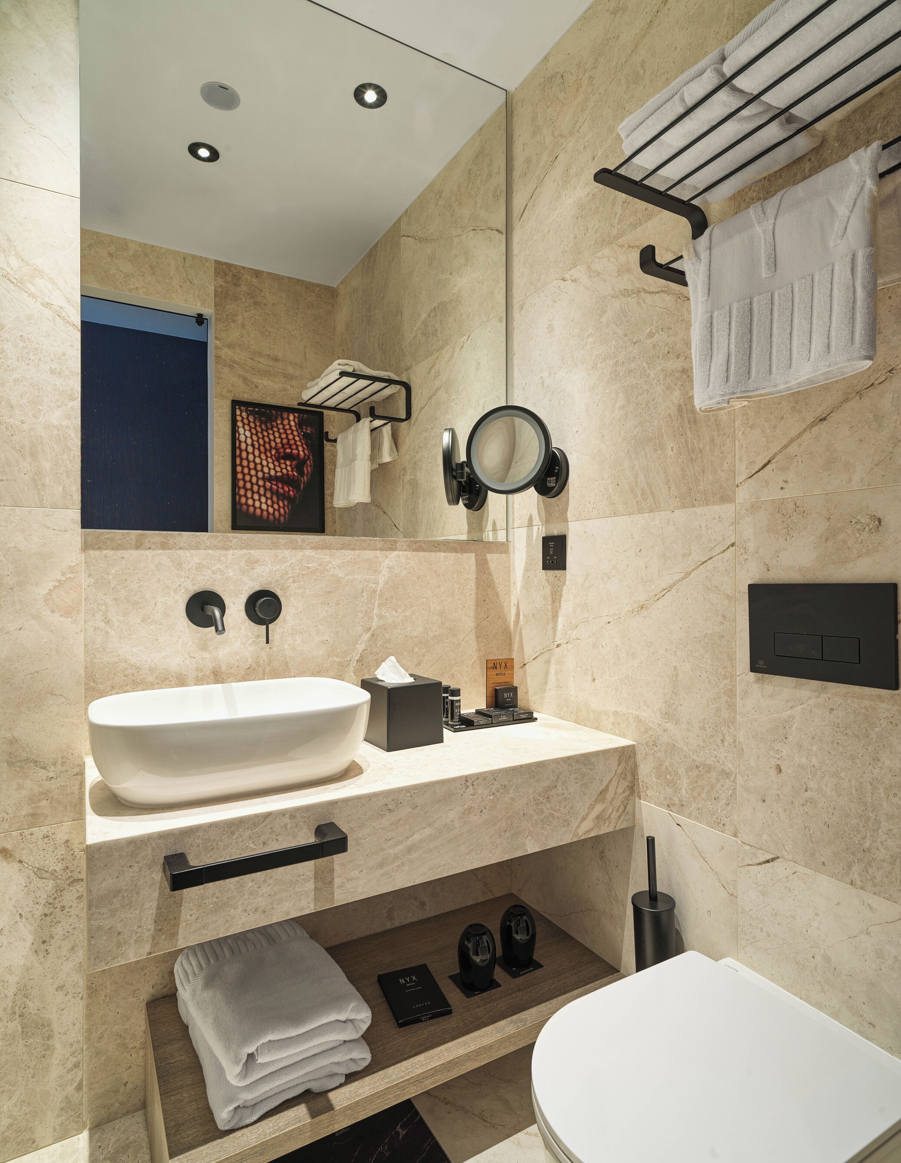 Un baño moderno con un lavamanos grande de color blanco, un espejo y un inodoro. Hay toallas y artículos de tocador en la encimera.